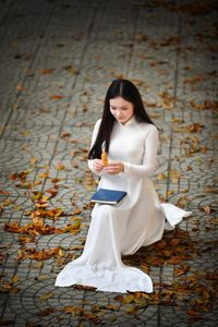 Elegant Vietnamese student in white Ao Dai reading, timeless beauty amidst classic architecture.-16